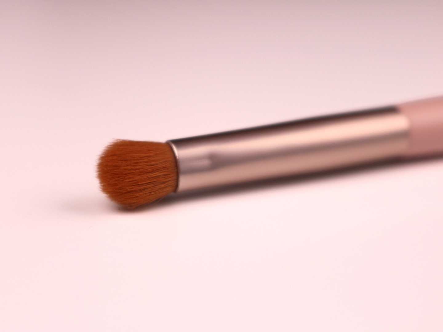 Makeup brush with brown bristles on a pink background