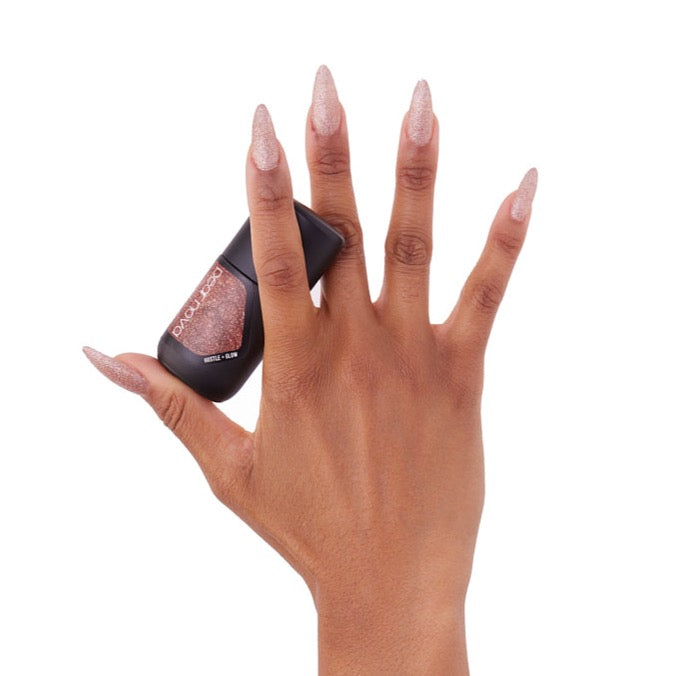 brown skin hand model holding bottle of nail lacquer with almond shaped gold glitter painted nails in Hustle + Glow