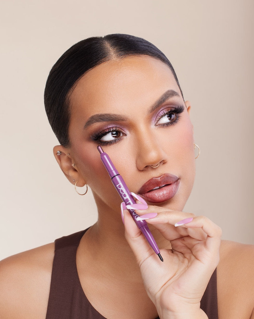 light brown skin model headshot with purple eye makeup and matching purple and white nails  holding eye duo stick 