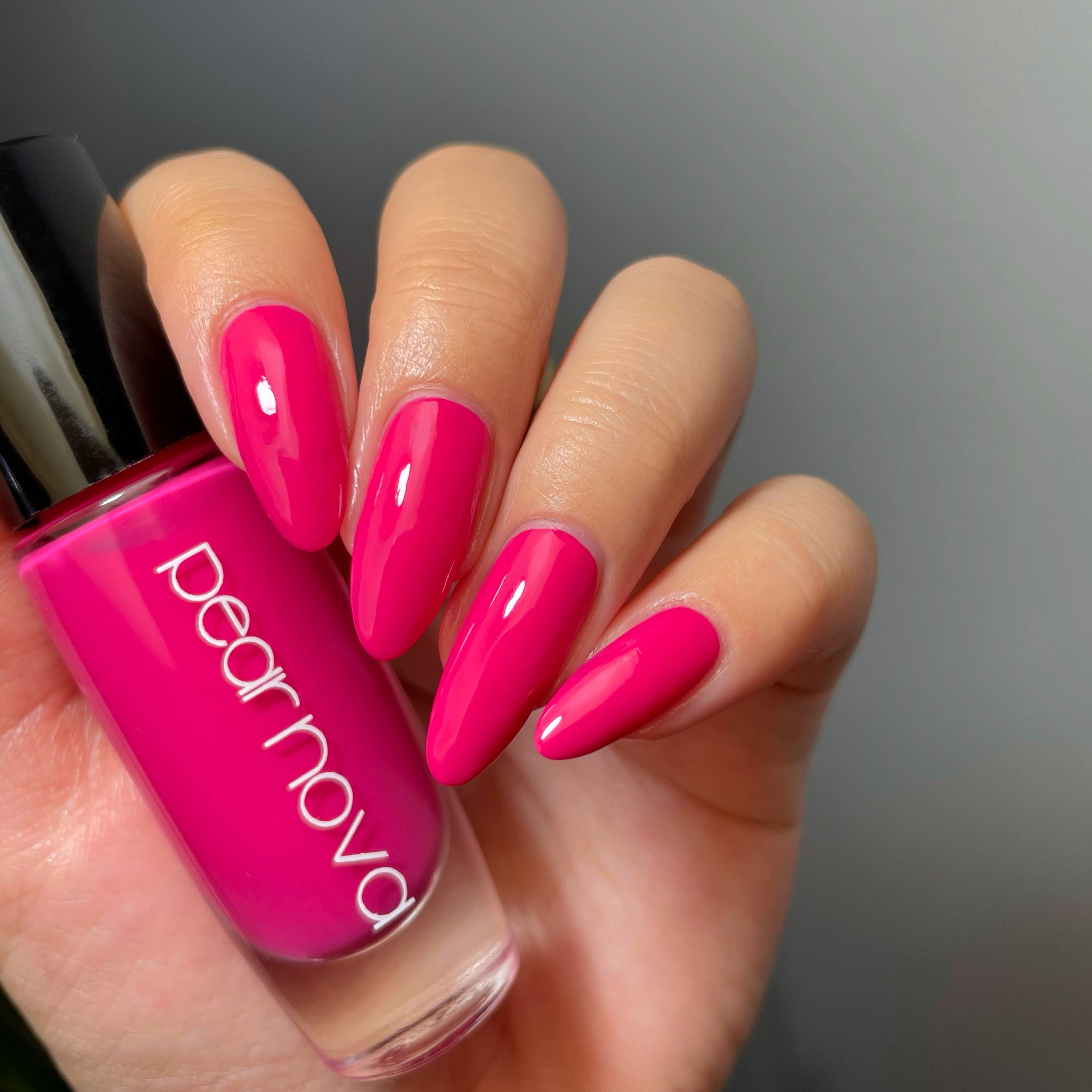 fair skin hand model holding bottle of nail polish with almond shaped nails painted